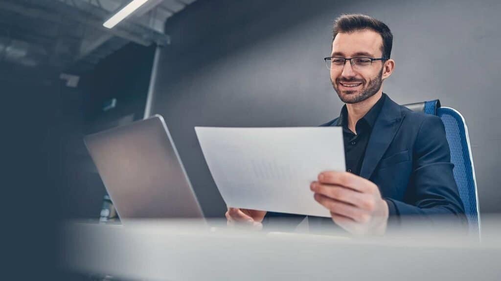 Professionel mand arbejdende med laptop og dokumenter på kontor, digitalt arbejde.