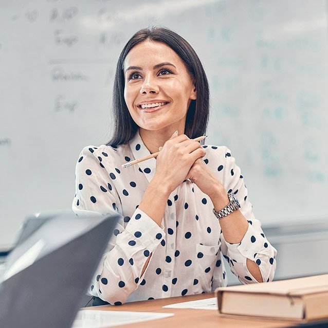 Kvindelig lærer i klasseværelse med skolematerialer og whiteboard.