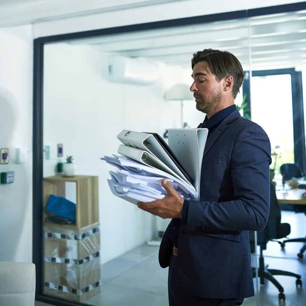 Håndholdt stak med papirer og mapper i kontormiljø, professionel forretningsmand i suits.