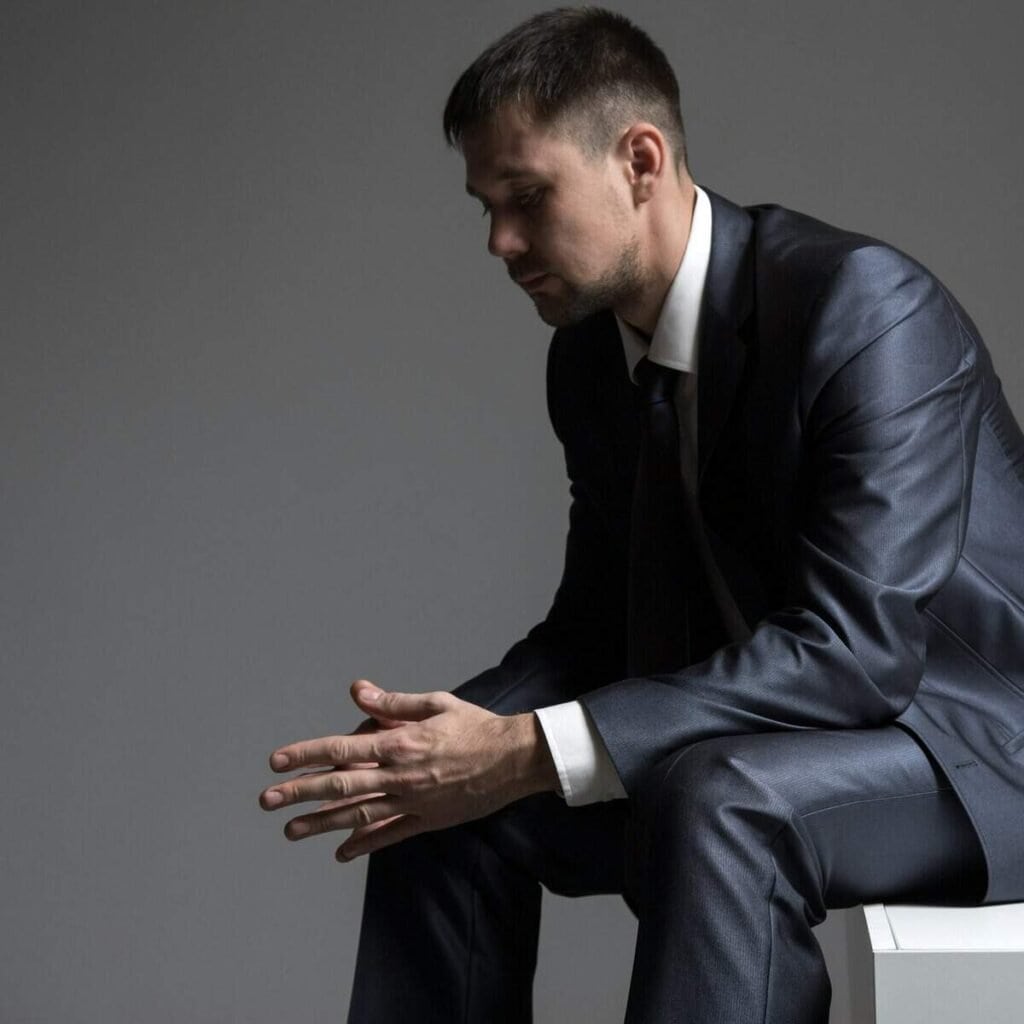 Selvreflekterende mand i sort jakkesæt, der sidder dybt i tanke, symboliserer professionalisme og introspektion.