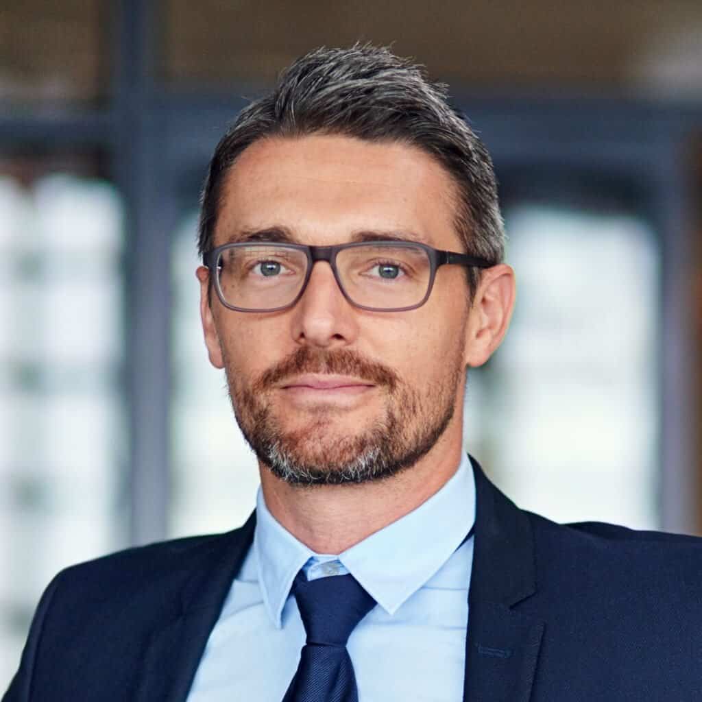 Innovativ forretningsmand i formiddagsmøde, iført jakkesæt og briller, professionel stil.