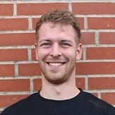 Menneske med smilende ansigt foran mursten væg.