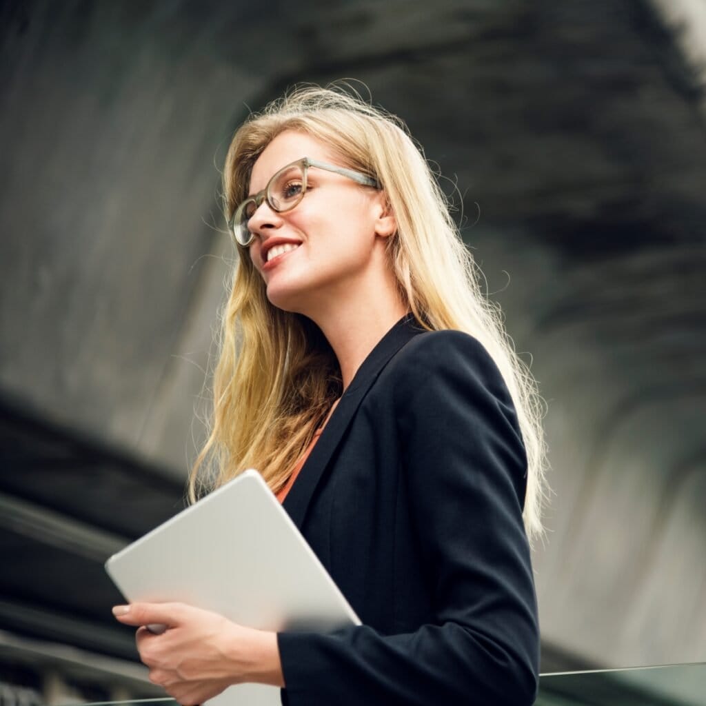 Moderne forretningskvinde med laptop under jernbanebro, professionel og selvsikker.
