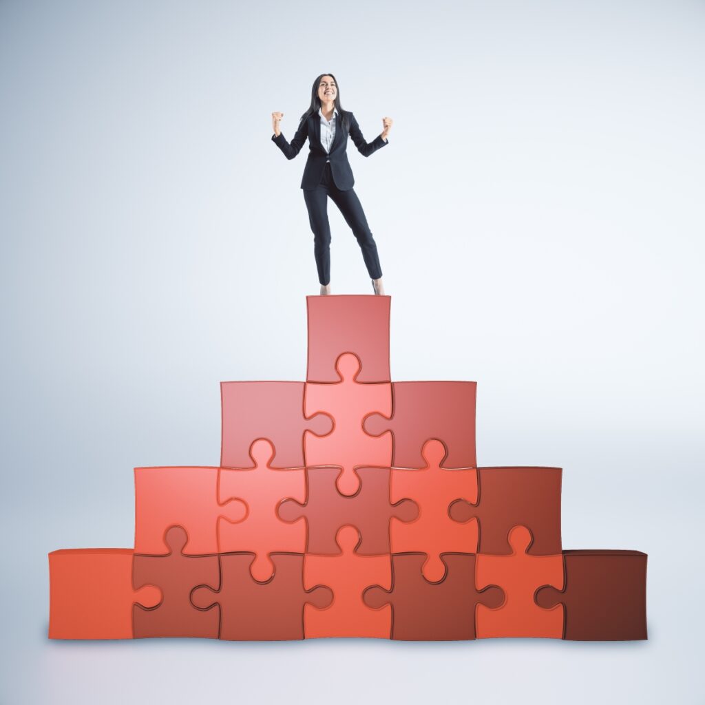 Kvinde i forretningsdragt står triumferende på puslespilsblokke, symboliserer ledelses- og teamudvik.