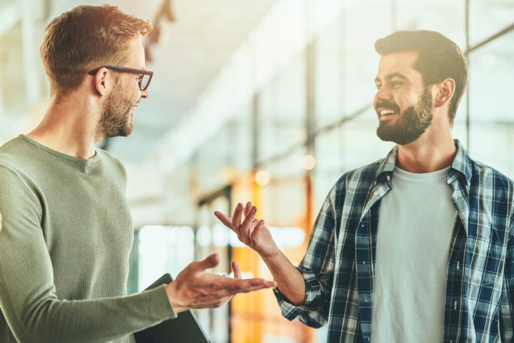 To mænd i samtale under medarbejdermøde i et lyst kontor.