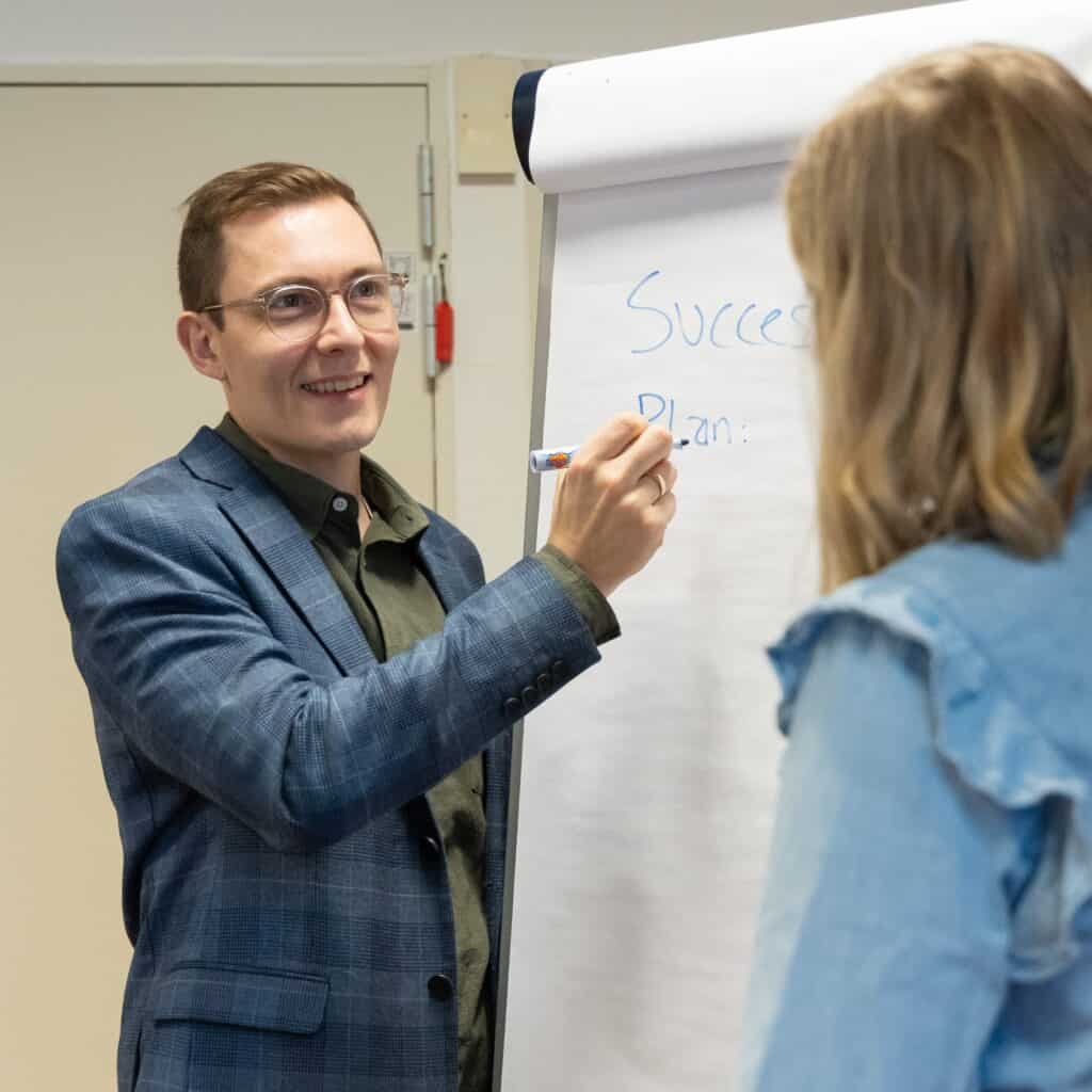 Mand holder præsentation foran kvinde ved whiteboard om forandringsledelse.