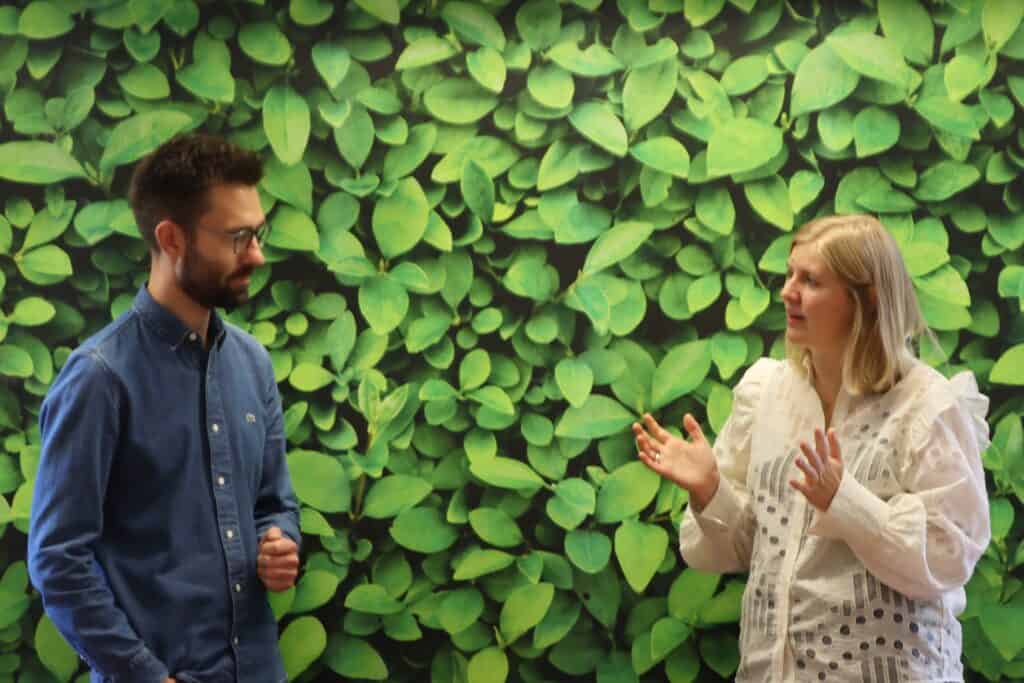 Medarbejdersamtale mellem to personer foran grøn væg, fokus på kommunikation og samarbejde.