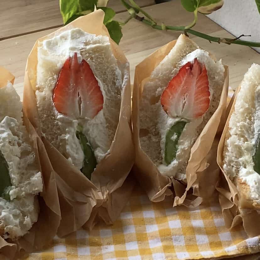 Fruit sando featuring one large whole strawberry cut into the shape of a flower nestled in soft white bread with creamy filling.