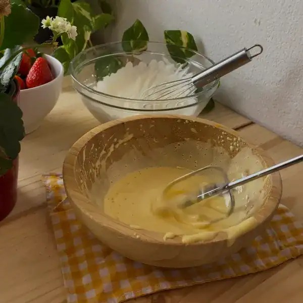 Beaten eggs with sugar in a bowl, whisked to a pale and creamy texture, essential for a light and airy strawberry tiramisu recipe.
