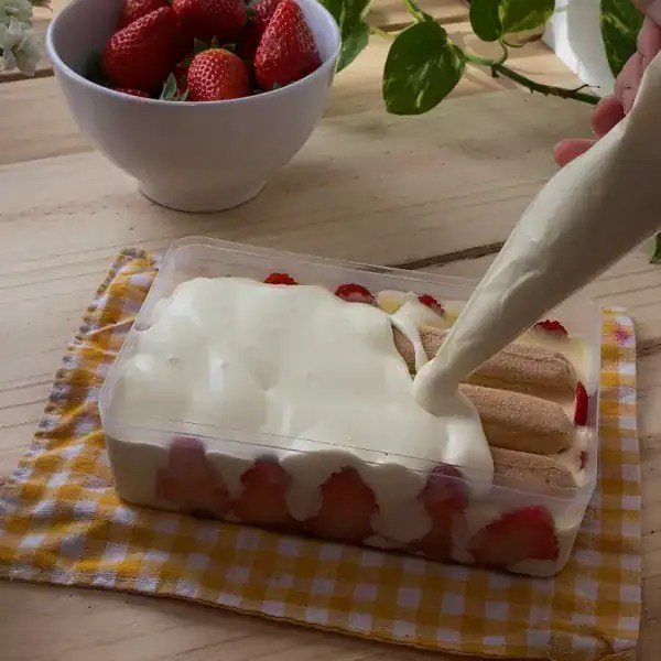 The final layer of smooth mascarpone cream being spread evenly on top of a strawberry tiramisu
