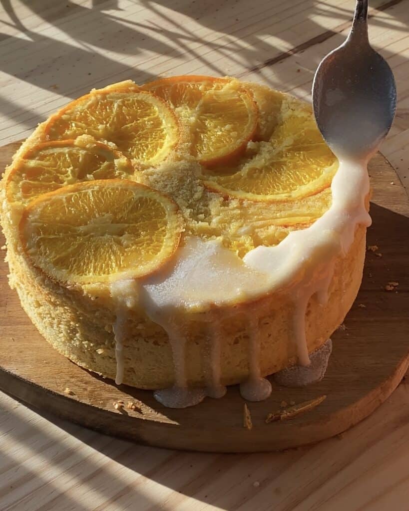 Close-up of a spoon pouring orange glaze over a moist upside-down orange cake, highlighting the glossy finish and vibrant citrus flavors