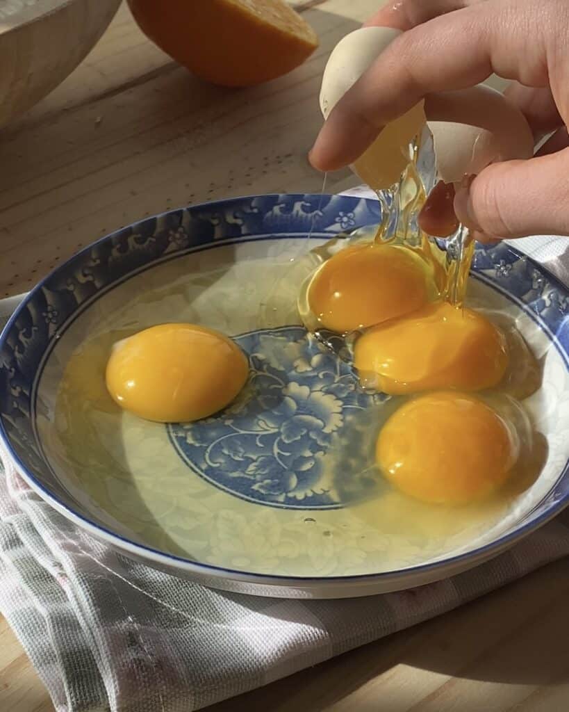 A close-up of eggs being cracked into a bowl, with yolks and whites visible, ready for mixing in a recipe.
