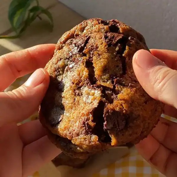A chocolate chip cookie being broken open, revealing melted chocolate inside.
