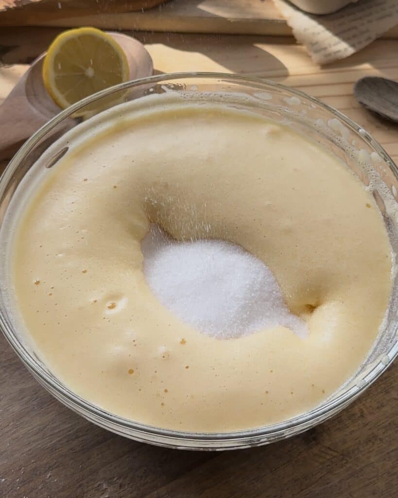 Adding sugar to the eggs while whisking, creating a sweet and smooth base for the cake layer in the homemade raspberry tiramisu