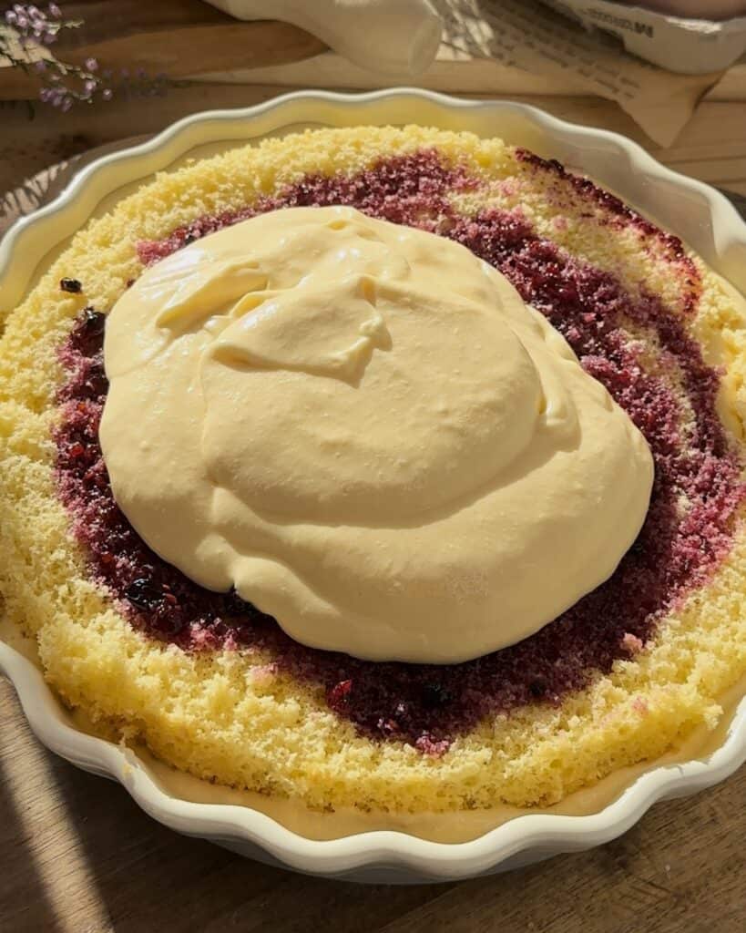 Adding a creamy layer of mascarpone filling over the cake, creating a rich and smooth base for the homemade raspberry tiramisu