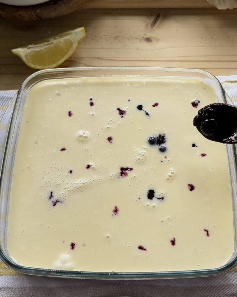 Spreading blueberry jam with a spoon over the irresistible blueberry cheesecake bars for a irresistible savor