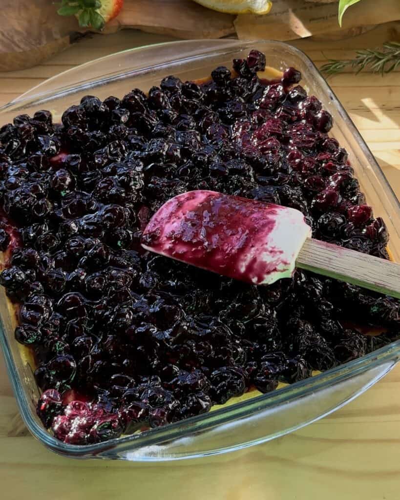 Spreading a luscious layer of blueberry jam over irresistible blueberry cheesecake bars for a delectable topping