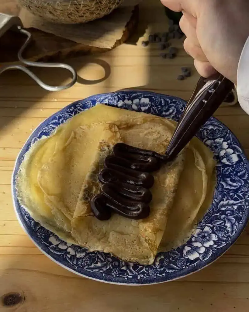 Filling the freshly cooked crepes with rich chocolate, preparing them to be rolled into delicious chocolate crepe rolls
