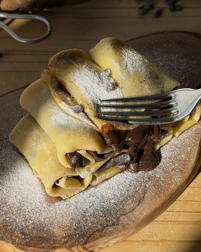 Adding a dusting of powdered sugar to the chocolate crepe rolls, enhancing their sweetness and ready to be enjoyed