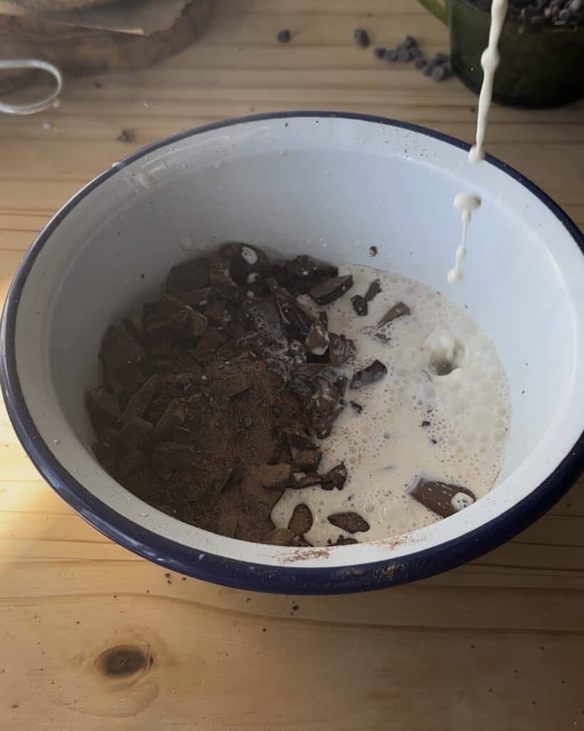 Adding heavy cream to the chopped chocolate to create a smooth, glossy ganache for topping the chocolate cake