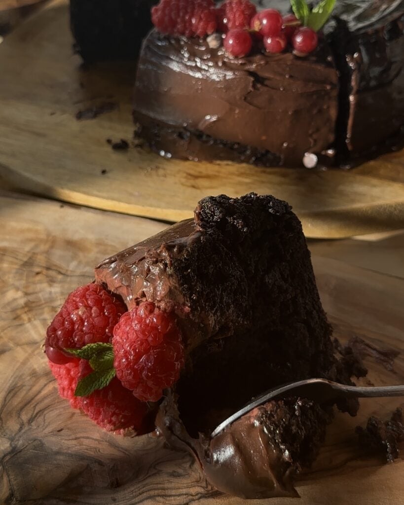 A portion of a perfect chocolate cake topped with fresh forest fruits, ready to be enjoyed with its rich, moist texture and vibrant fruit contrast