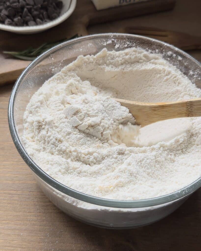 Mixing sugar, flour, and baking powder together to create the dry ingredient base for the chocolate chip muffins