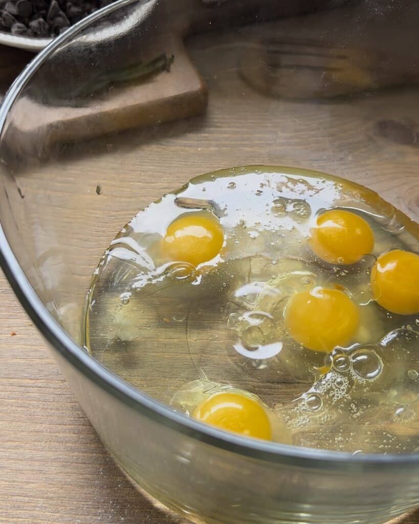 Cracking fresh eggs into a bowl, preparing them as part of the wet ingredients for the chocolate chip muffins batter