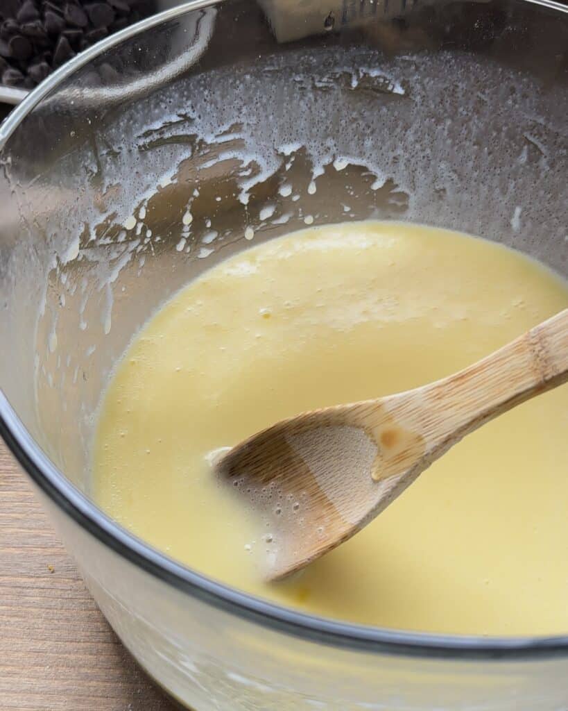 Whisking eggs, oil, and milk together to create a smooth, liquid mixture for the chocolate chip muffins batter.
