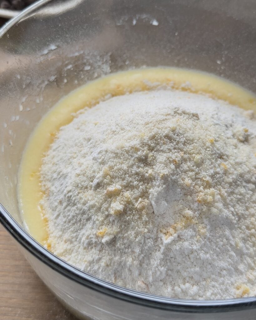 Folding the dry ingredients into the wet mixture and gently mixing them together to create a smooth batter for the chocolate chip muffins