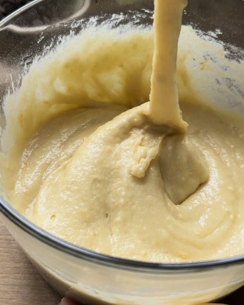 Folding the dry ingredients into the wet mixture and gently mixing them together to create a smooth batter for the chocolate chip muffins