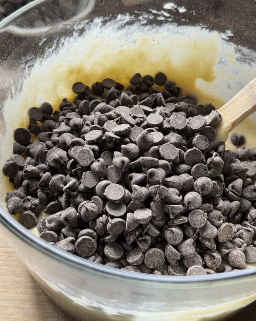 Adding chocolate chips to the batter, folding them in evenly to ensure every bite of the chocolate chip muffins is rich and delicious