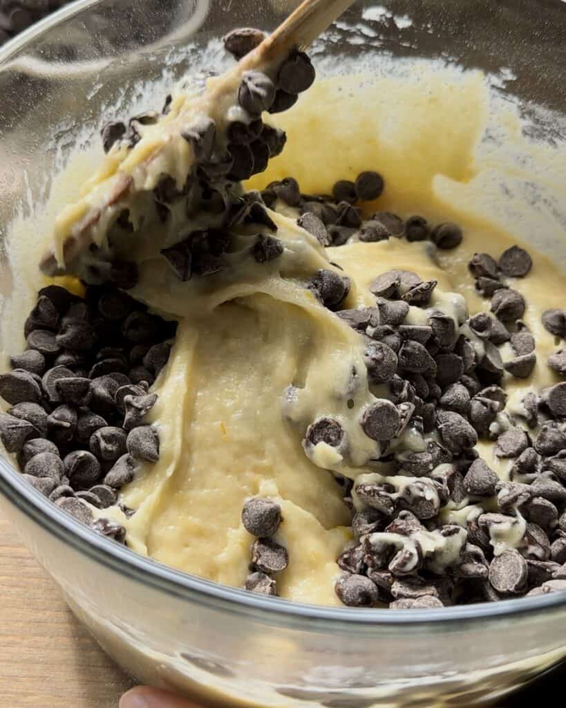 Adding chocolate chips to the batter, folding them in evenly to ensure every bite of the chocolate chip muffins is rich and delicious