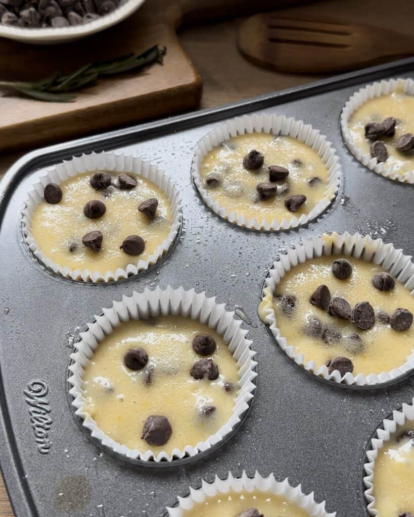 Chocolate chip muffin batter in a muffin tin, ready to be baked until golden brown and filled with melty chocolate chips