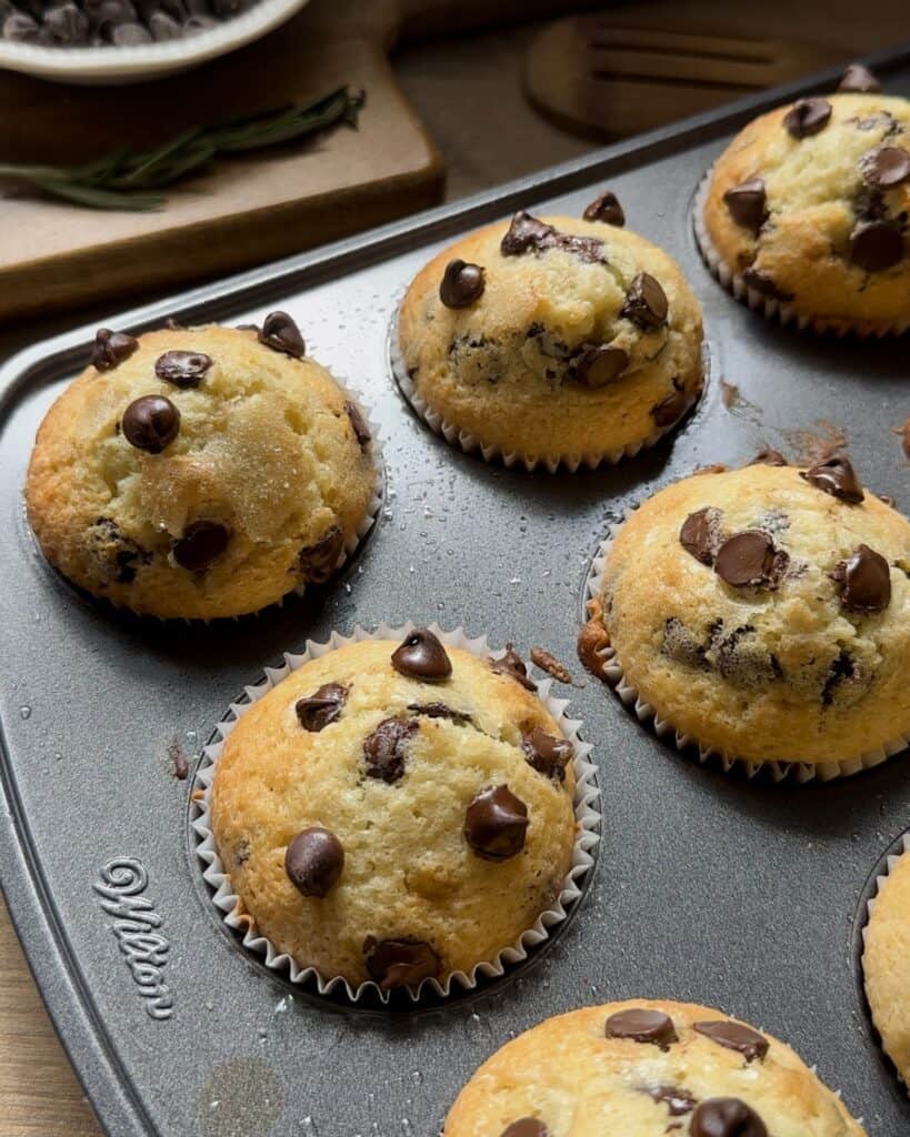 Freshly baked chocolate chip muffins, golden brown with melted chocolate chips, cooling and ready to enjoy