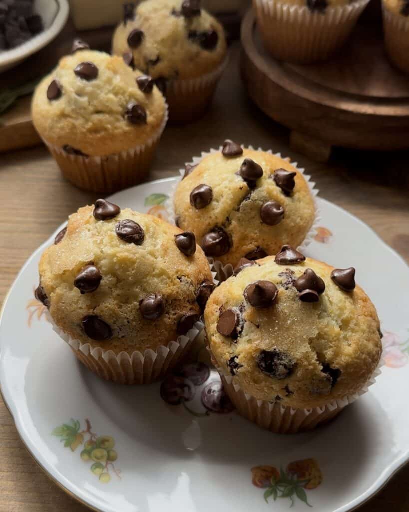 Freshly baked chocolate chip muffins, golden brown with melted chocolate chips, cooling and ready to enjoy