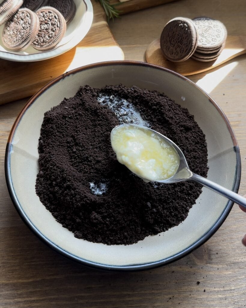 Mixing crushed Oreo biscuits with melted butter to create a rich, buttery base for the no-bake Oreo cheesecake
