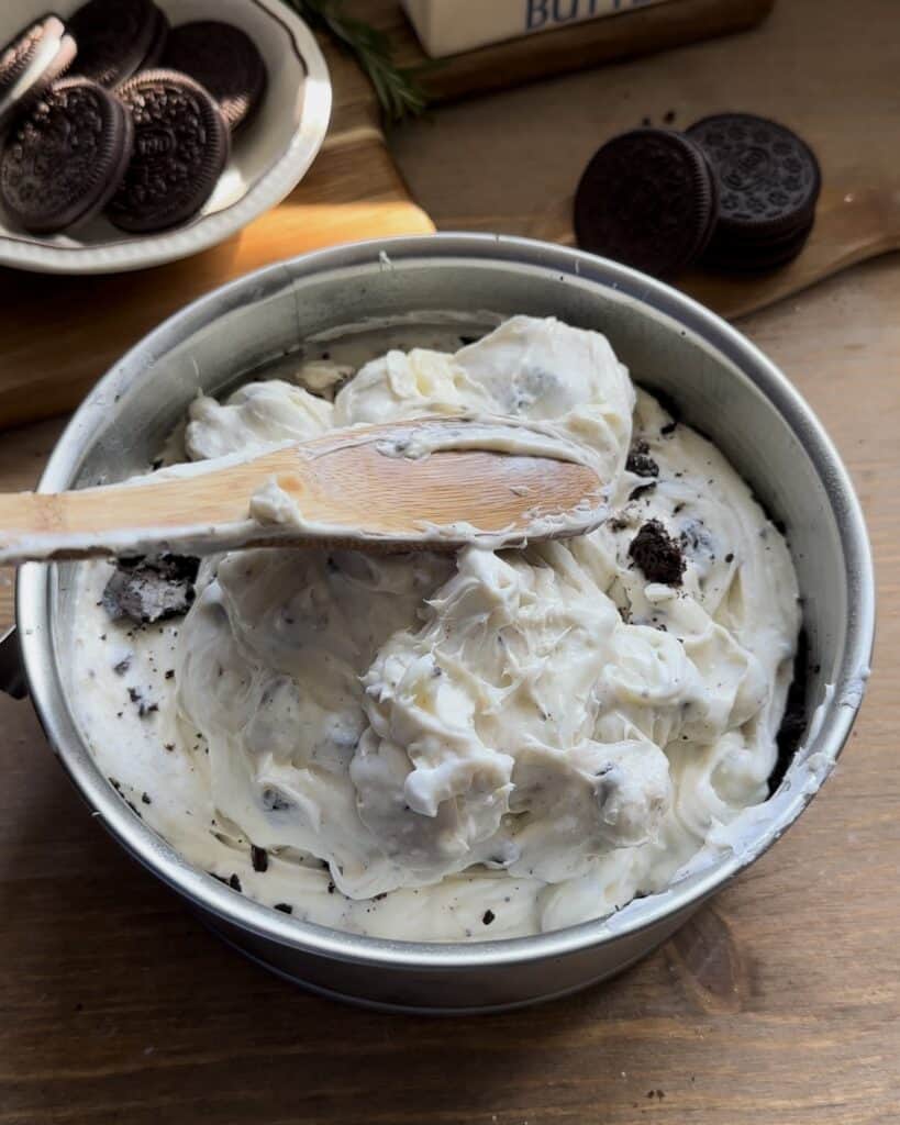 Carefully filling the mold with the cream cheese mixture, mixed with chopped Oreo cookies, to create the filling for the no-bake Oreo cheesecake