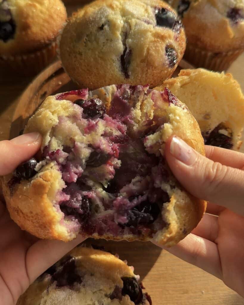 Freshly baked bakery-style blueberry lemon muffin cut in half, revealing a moist, fluffy interior filled with juicy blueberries and a touch of lemon zest