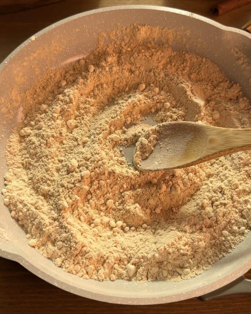 Toasting flour and dry milk powder in a saucepan to enhance the flavor for the Christmas cookie dough cheesecake batter.