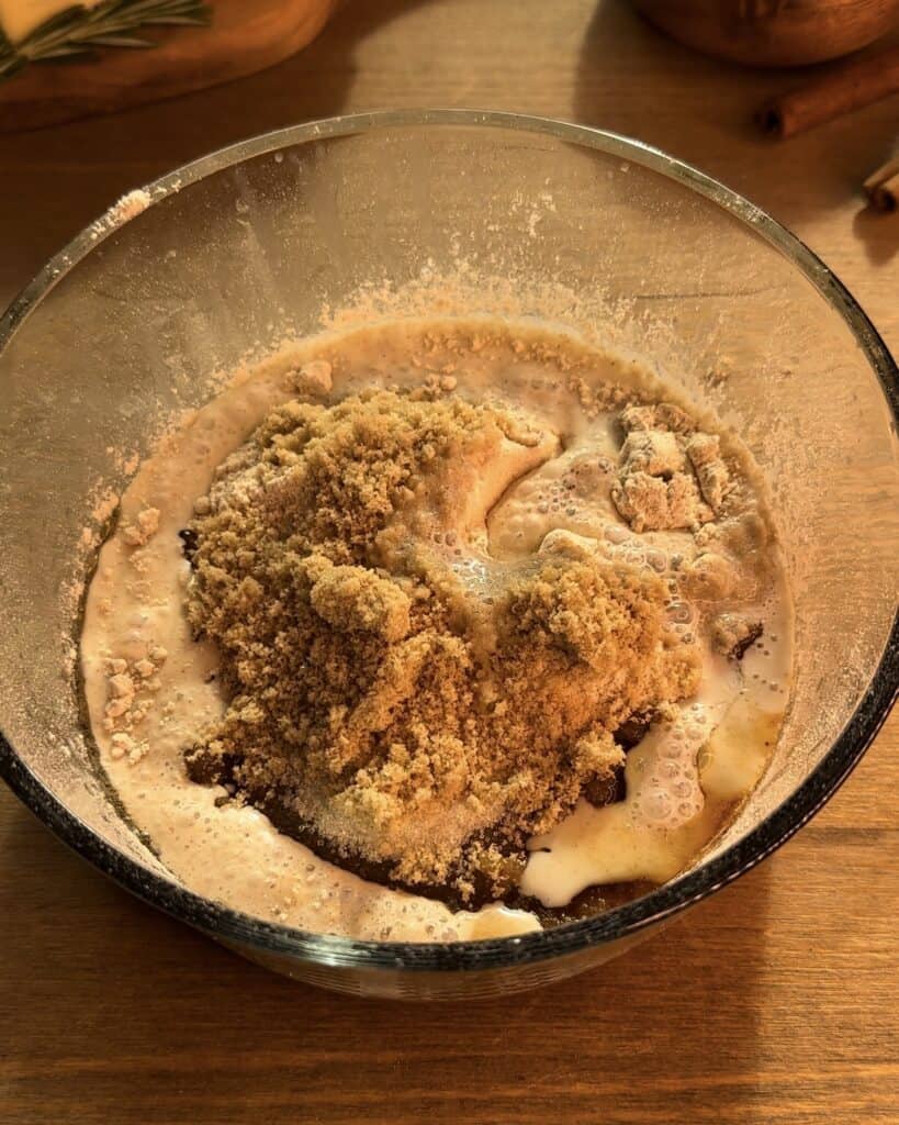 Mixing cooled brown butter, granulated sugar, brown sugar, milk, flour, and milk powder with a wooden spoon in a bowl to make the Christmas cookie dough cheesecake batter.