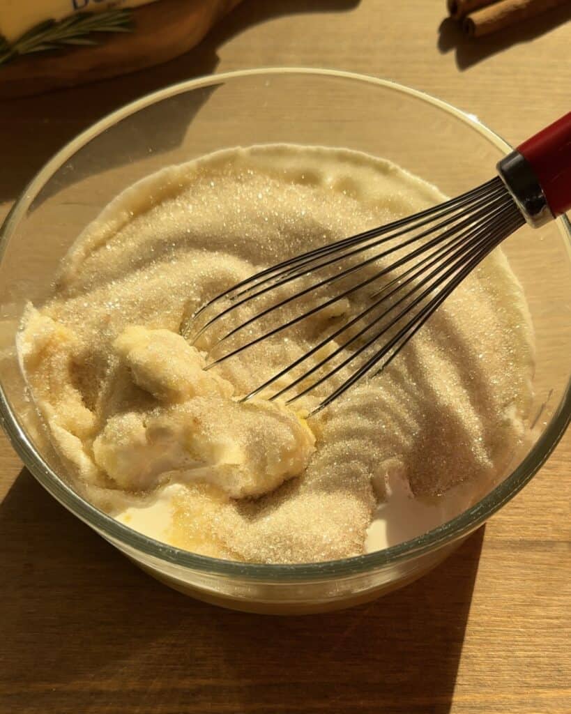 Mixing cream cheese, granulated sugar, heavy whipping cream, and eggs with a whisk in a bowl to create a smooth and creamy batter for the Christmas cookie dough cheesecake.