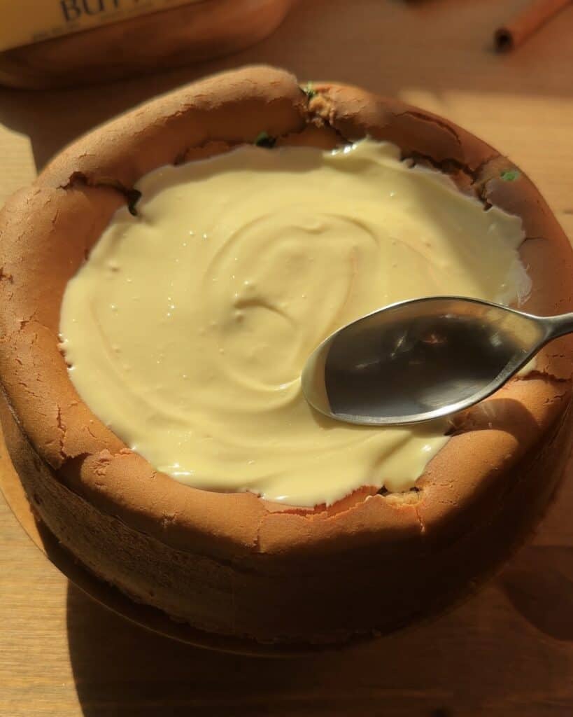 Christmas cookie dough cheesecake with a creamy texture, topped with freshly melted white chocolate spread with a spoon. The cheesecake has a cookie dough crust, is packed with red and green M&M’s inside, and exudes festive holiday vibes.