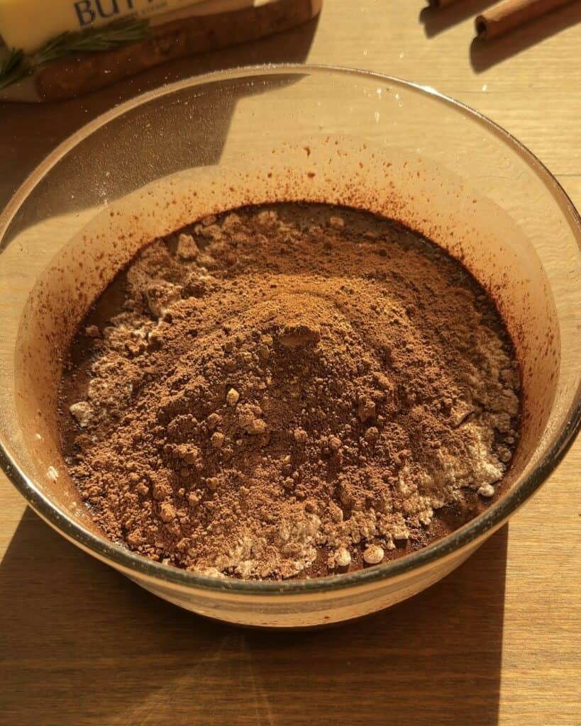 Adding cocoa powder to the Christmas brownies batter in a bowl with the rest of the ingredients, creating a rich, velvety, and creamy brownie batter perfect for the holiday season.