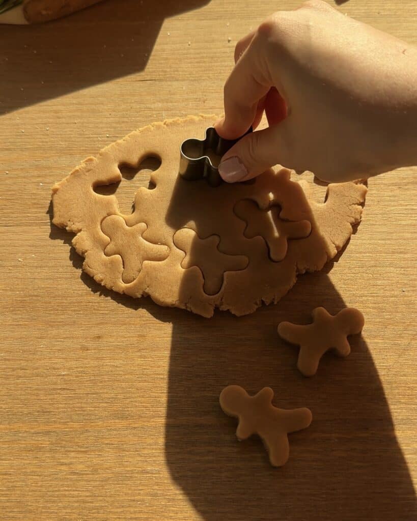 Cutting gingerbread cookies with a gingerbread-shaped mold on a wooden table to create festive toppings for Christmas brownies, perfect for the holiday season.