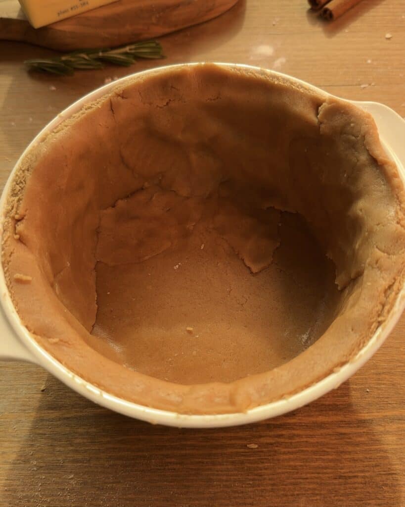 Gingerbread cookie dough in a greased pie mold, forming the spiced crust for a delicious Gingerbread Apple Pie with Cranberries on top to decorate