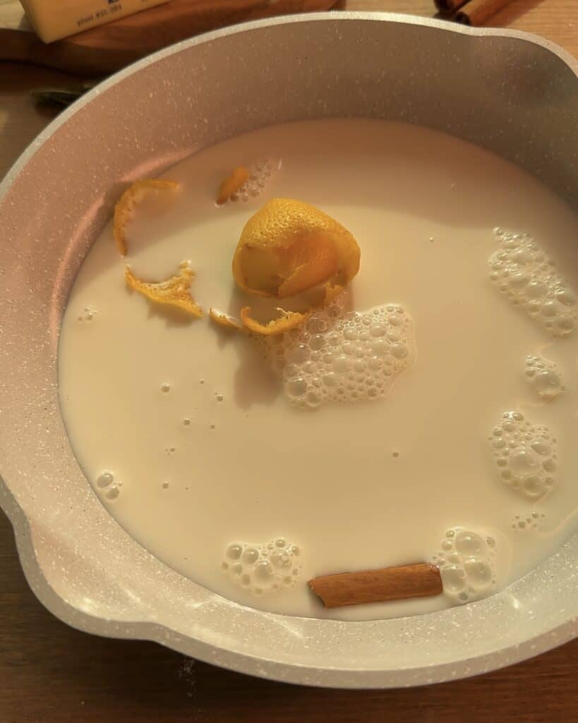 Preparing creamy custard in a pan with milk, lemon peel, sugar, and a cinnamon stick for the perfect Gingerbread Apple Pie