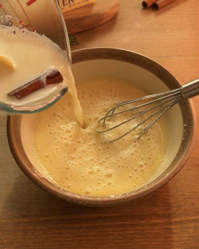 Pouring the infused milk with lemon peel, sugar, and cinnamon into the egg mixture to create a rich custard for the Gingerbread Apple Pie