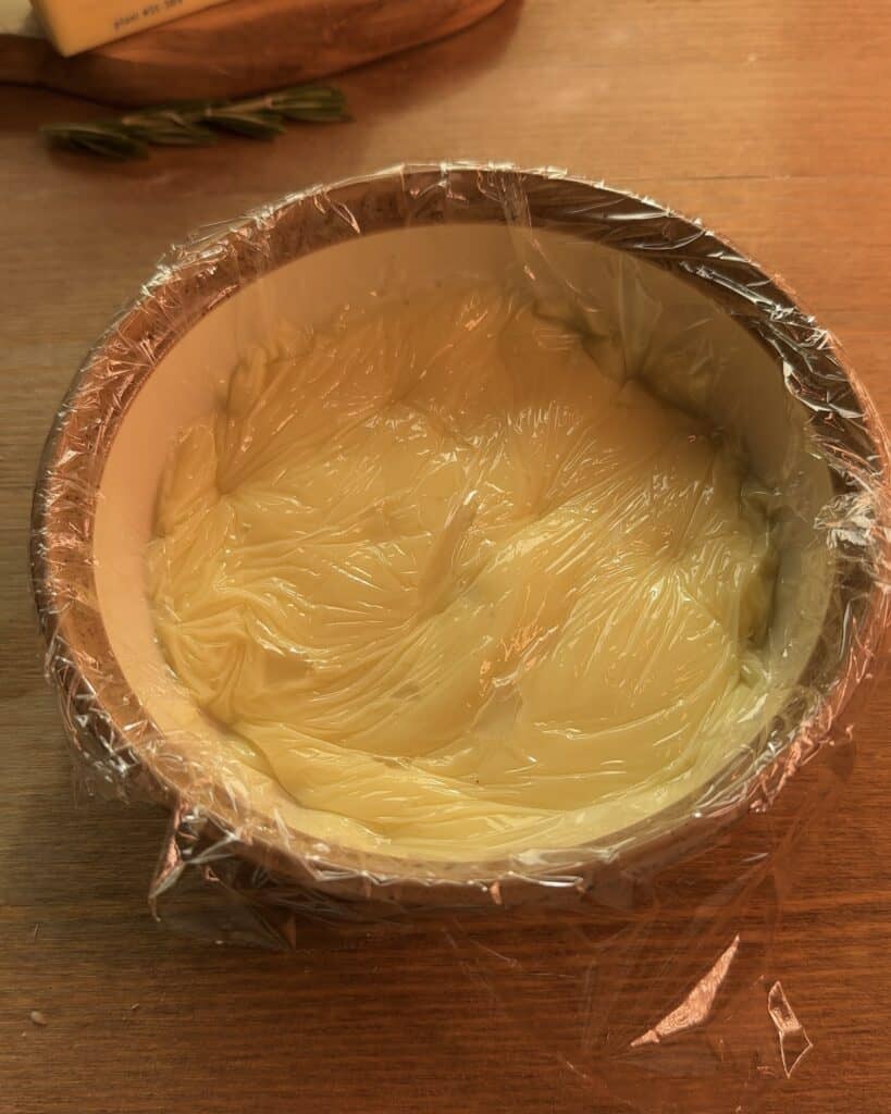 Smooth custard covered with plastic wrap in a bowl to prevent skin formation, ready for the Gingerbread Apple Pie