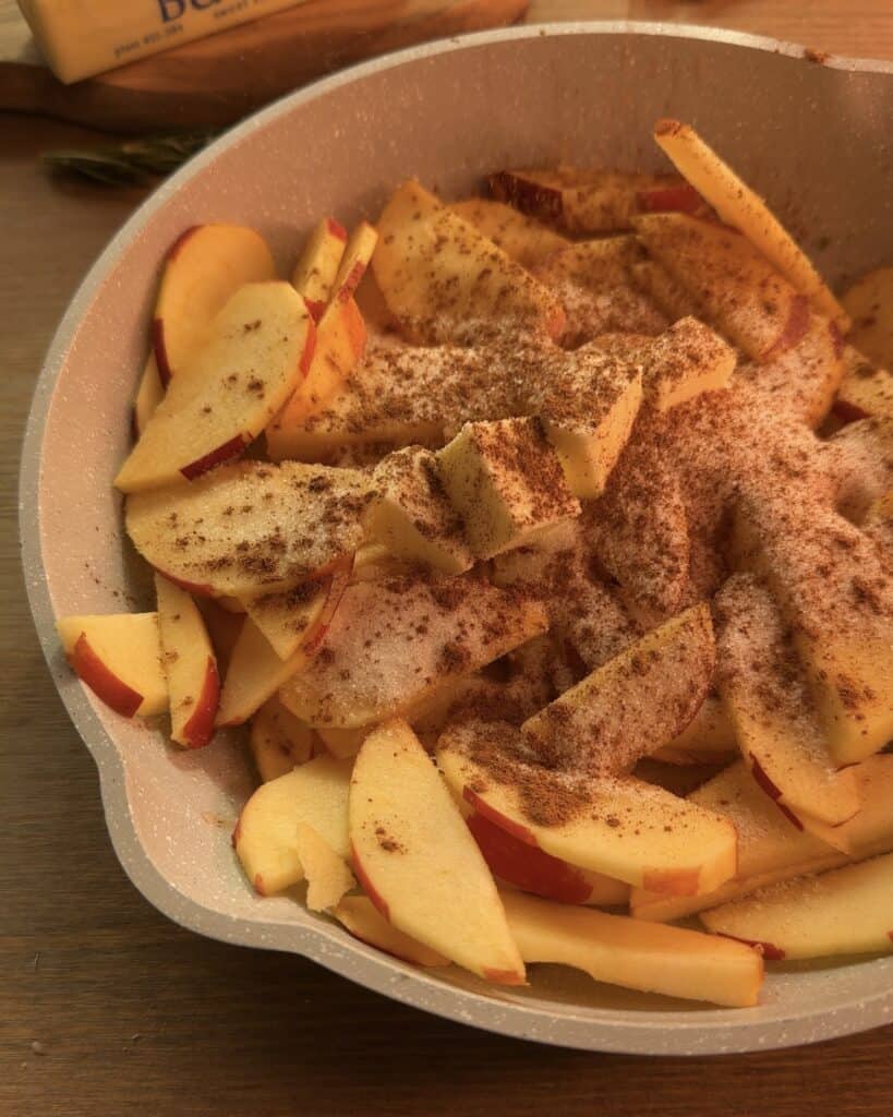 Cooking sliced apples with granulated sugar, ground cinnamon, and butter in a saucepan until tender for the Gingerbread Apple Pie