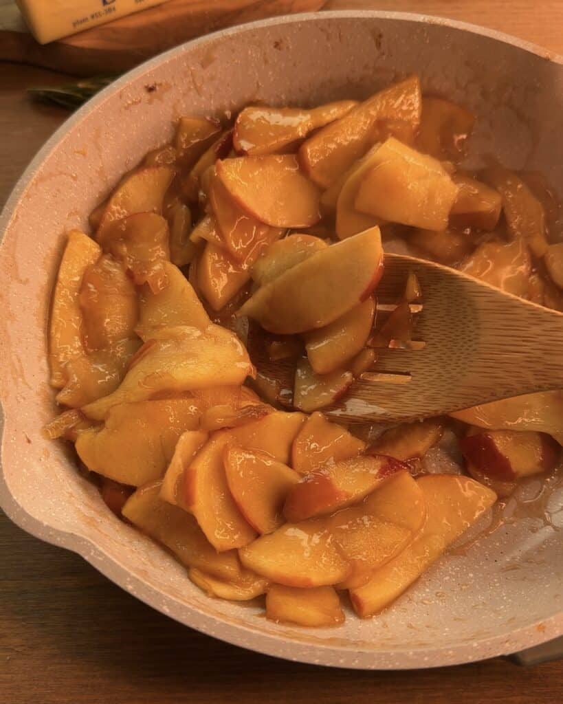 Cooking sliced apples with granulated sugar, ground cinnamon, and butter in a saucepan until tender for the Gingerbread Apple Pie